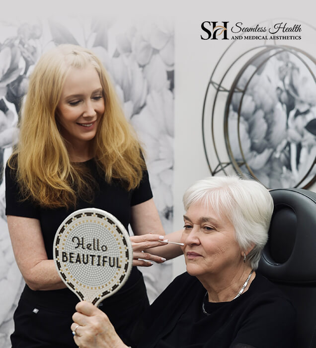 Mature patient smiling at a hand mirror after her treatment with a Seamless Health injector